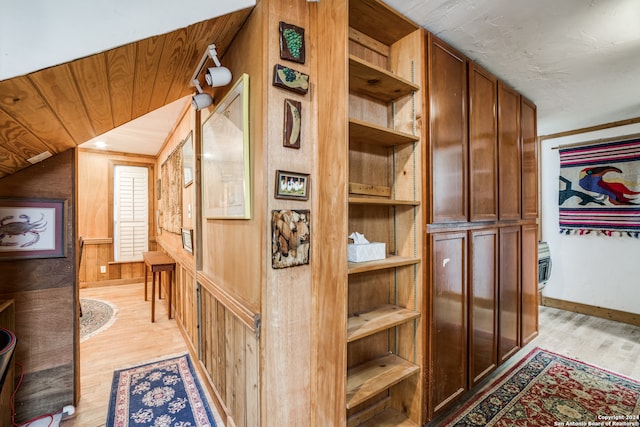 interior space featuring light hardwood / wood-style floors, wood walls, and lofted ceiling