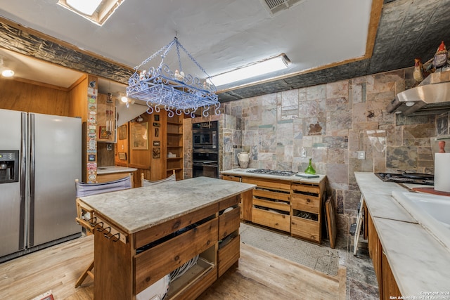 kitchen with tile walls, light wood-type flooring, appliances with stainless steel finishes, and a center island