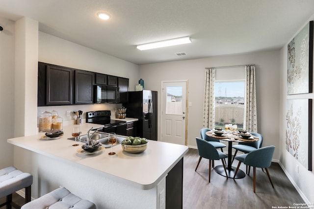 kitchen featuring black appliances, kitchen peninsula, a kitchen bar, and light hardwood / wood-style floors