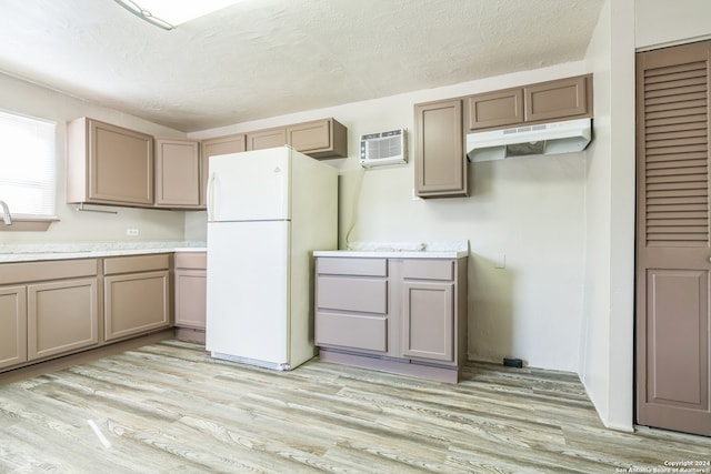 kitchen featuring a wall unit AC, light hardwood / wood-style floors, a textured ceiling, sink, and white fridge