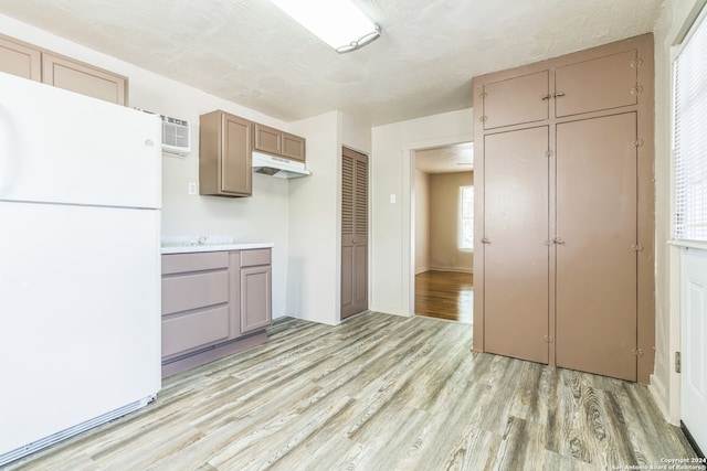 kitchen with white refrigerator, a textured ceiling, a wall unit AC, and light hardwood / wood-style flooring