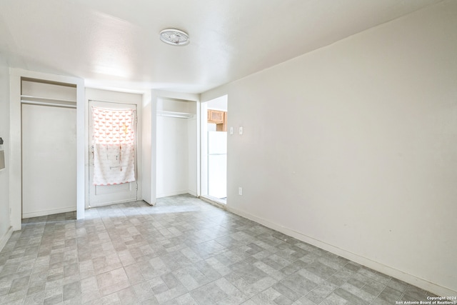 unfurnished bedroom featuring multiple windows, white refrigerator, and two closets