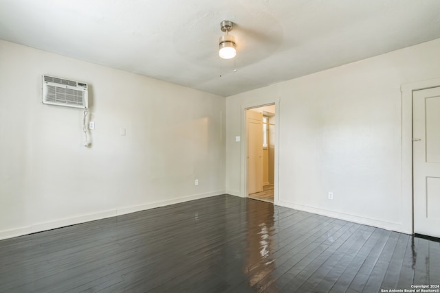 unfurnished room featuring dark wood-type flooring, a wall unit AC, and ceiling fan