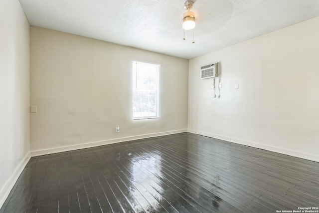 empty room with a wall mounted AC, a textured ceiling, dark wood-type flooring, and ceiling fan