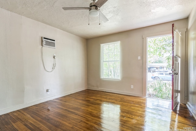 empty room featuring dark wood-type flooring, a wall unit AC, ceiling fan, and a textured ceiling