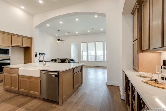 kitchen with stainless steel appliances, sink, a kitchen island with sink, ceiling fan, and light wood-type flooring