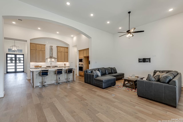 living room with ceiling fan with notable chandelier, sink, light hardwood / wood-style flooring, and high vaulted ceiling