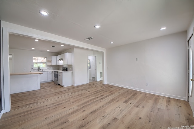 kitchen featuring sink, tasteful backsplash, white cabinetry, light hardwood / wood-style flooring, and stainless steel electric range oven