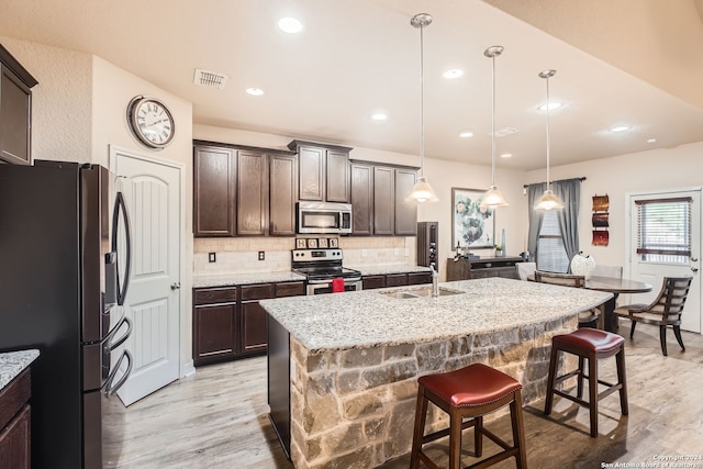 kitchen with appliances with stainless steel finishes, sink, an island with sink, and light hardwood / wood-style flooring