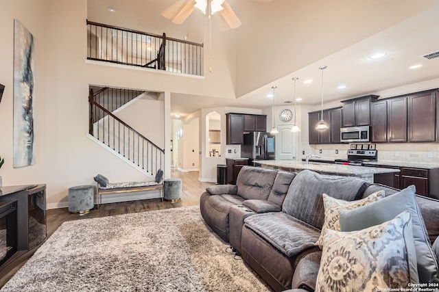 living room featuring dark wood-type flooring, a high ceiling, and ceiling fan