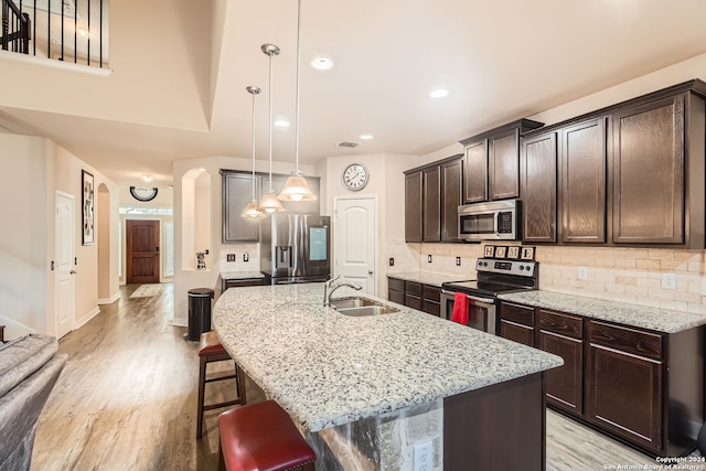 kitchen with stainless steel appliances, hanging light fixtures, sink, a kitchen breakfast bar, and a kitchen island with sink