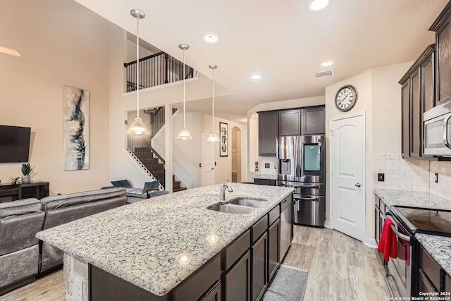 kitchen with sink, a kitchen island with sink, light wood-type flooring, appliances with stainless steel finishes, and decorative light fixtures