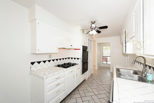 kitchen with tile counters, black appliances, white cabinetry, and sink