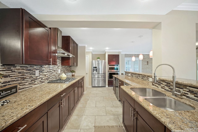 kitchen with light stone counters, stainless steel appliances, wall chimney range hood, pendant lighting, and sink