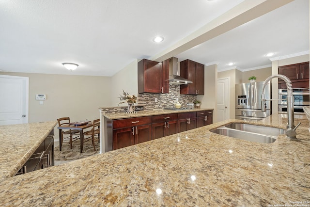 kitchen featuring light stone counters, sink, tasteful backsplash, wall chimney range hood, and appliances with stainless steel finishes