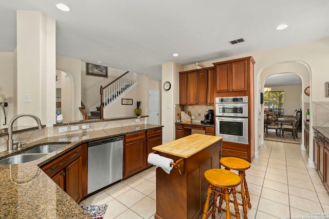 kitchen with stainless steel appliances, light tile patterned flooring, dark stone counters, and sink