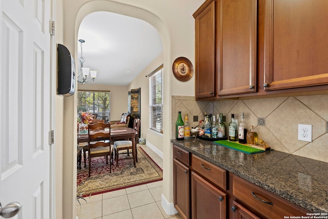 kitchen featuring decorative backsplash, dark stone counters, light tile patterned floors, and an inviting chandelier