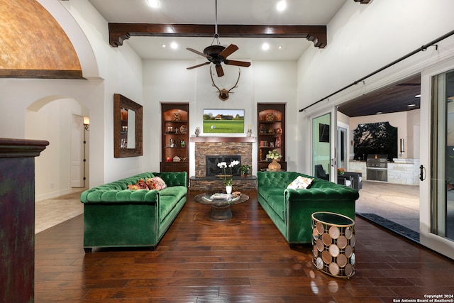 living room featuring dark hardwood / wood-style flooring, a stone fireplace, beam ceiling, and built in shelves