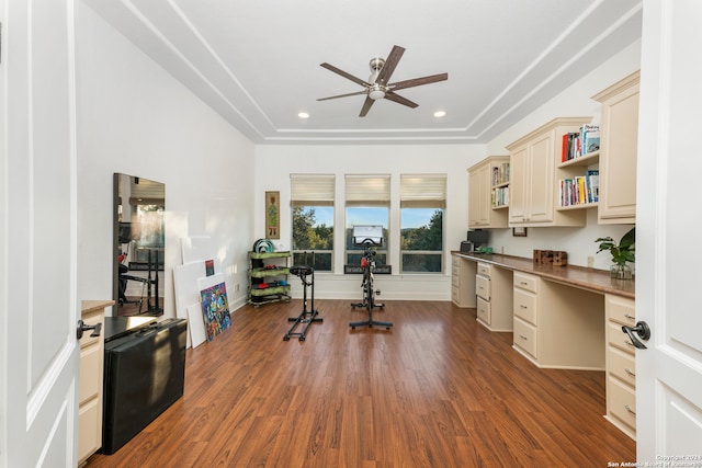 home office featuring dark hardwood / wood-style flooring, a tray ceiling, built in desk, and ceiling fan