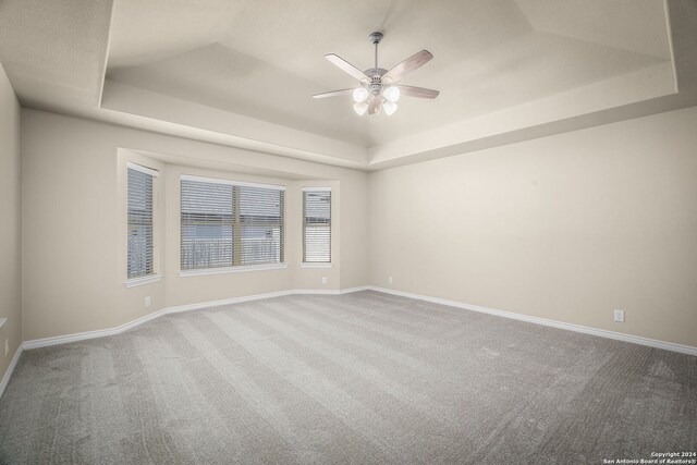 carpeted empty room with ceiling fan and a tray ceiling