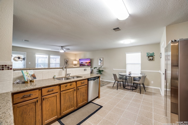 kitchen with a textured ceiling, sink, ceiling fan, light stone countertops, and appliances with stainless steel finishes