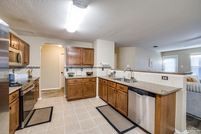 12750 Rambling Rose, San Antonio, TX 78253 - kitchen with stainless steel appliances, a sink, brown cabinetry, a peninsula, and tasteful backsplash