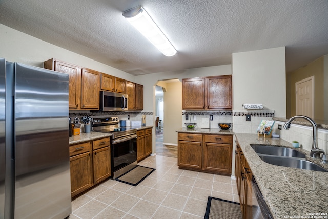 kitchen with sink, appliances with stainless steel finishes, tasteful backsplash, light stone countertops, and a textured ceiling