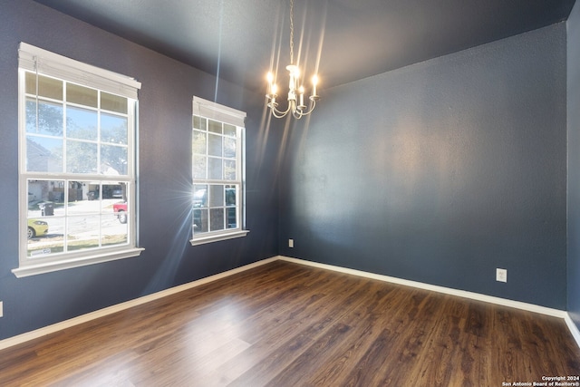 spare room featuring dark wood-type flooring and a notable chandelier