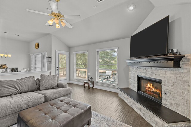 living room featuring a stone fireplace, hardwood / wood-style floors, ceiling fan with notable chandelier, and vaulted ceiling