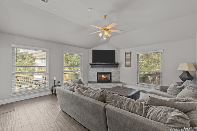 living room featuring a stone fireplace, lofted ceiling, and ceiling fan