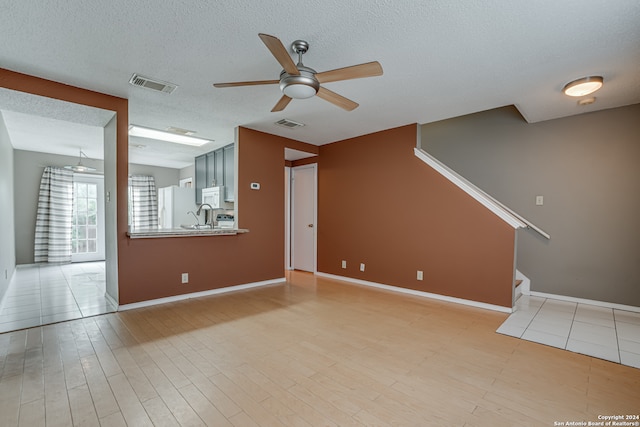 unfurnished living room featuring light wood-type flooring, a textured ceiling, and ceiling fan