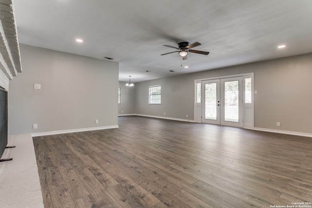 unfurnished living room with a fireplace, french doors, dark wood-type flooring, and ceiling fan with notable chandelier