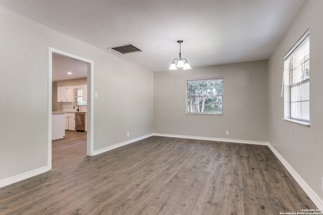 unfurnished room with sink, hardwood / wood-style floors, a healthy amount of sunlight, and a notable chandelier