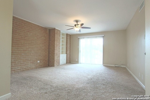 carpeted empty room with ceiling fan and brick wall