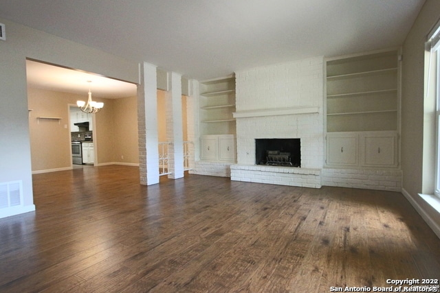 unfurnished living room featuring built in shelves, a fireplace, dark hardwood / wood-style floors, and an inviting chandelier