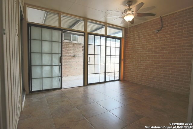 unfurnished room with tile patterned flooring, brick wall, and ceiling fan