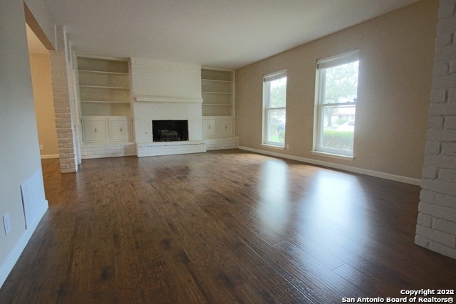 unfurnished living room with dark wood-type flooring and built in features