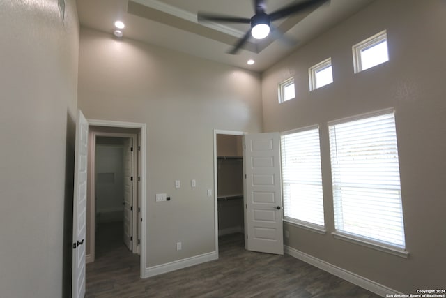 unfurnished bedroom featuring multiple windows, a spacious closet, dark hardwood / wood-style flooring, and ceiling fan