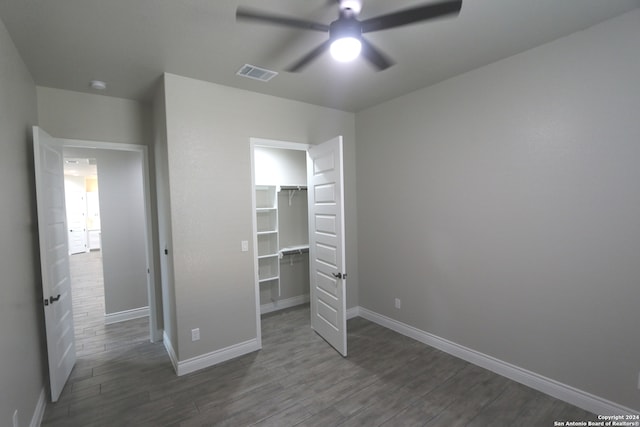 unfurnished bedroom with a walk in closet, ceiling fan, a closet, and dark hardwood / wood-style floors