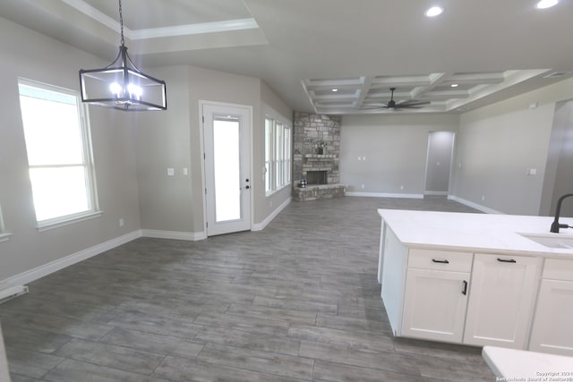 kitchen with light stone counters, a fireplace, coffered ceiling, decorative light fixtures, and white cabinets