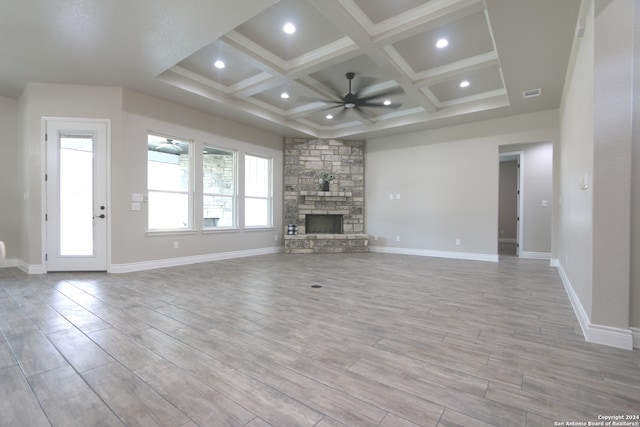 unfurnished living room with coffered ceiling, a stone fireplace, ceiling fan, light wood-type flooring, and beamed ceiling