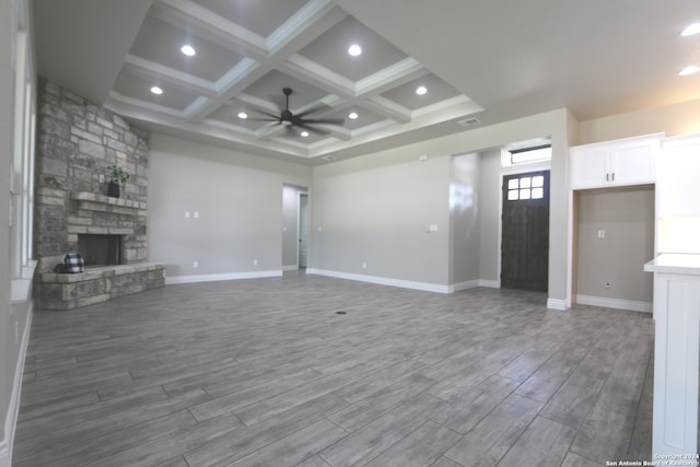 unfurnished living room with beamed ceiling, hardwood / wood-style floors, a stone fireplace, and coffered ceiling