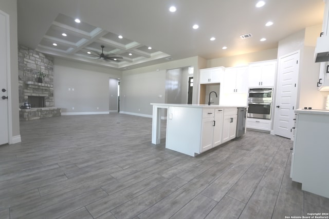 kitchen with a fireplace, a center island with sink, white cabinets, and light hardwood / wood-style flooring