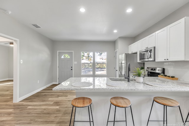 kitchen featuring light stone counters, white cabinetry, appliances with stainless steel finishes, light hardwood / wood-style floors, and a kitchen breakfast bar