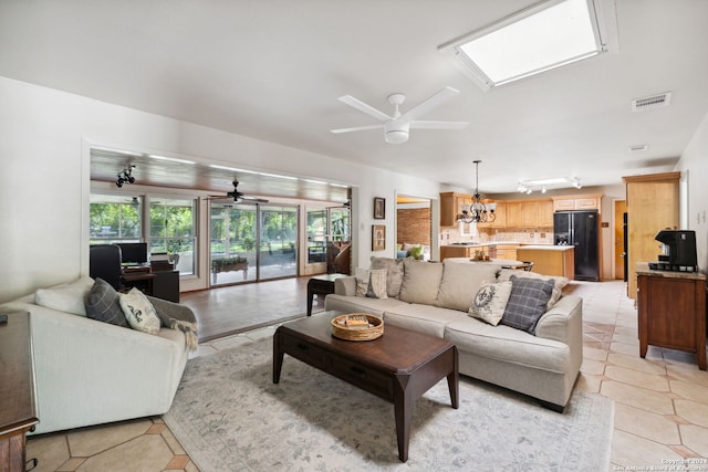 living room featuring ceiling fan with notable chandelier, a skylight, and light tile patterned flooring