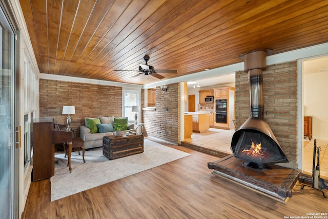 living room with a wood stove, ceiling fan, brick wall, wood ceiling, and light wood-type flooring