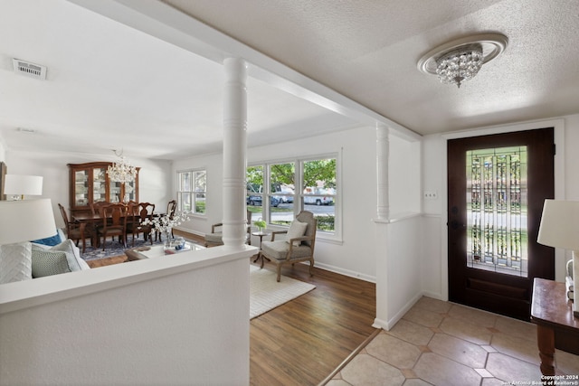 foyer with wood-type flooring, a textured ceiling, decorative columns, and an inviting chandelier