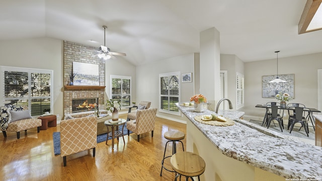 kitchen featuring light stone counters, light hardwood / wood-style flooring, lofted ceiling, a brick fireplace, and pendant lighting