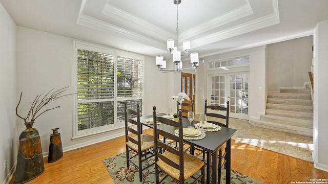 dining space featuring a tray ceiling, a notable chandelier, light hardwood / wood-style floors, and crown molding