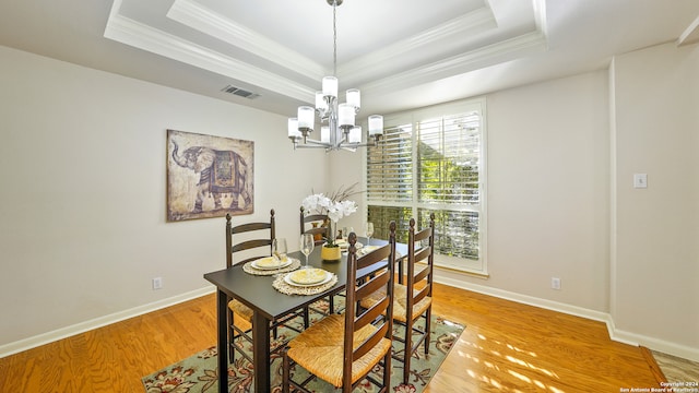 dining room featuring a notable chandelier, light hardwood / wood-style floors, and a raised ceiling